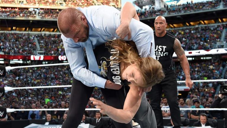 Rousey hiptosses Triple H from the ring as The Rock looks on