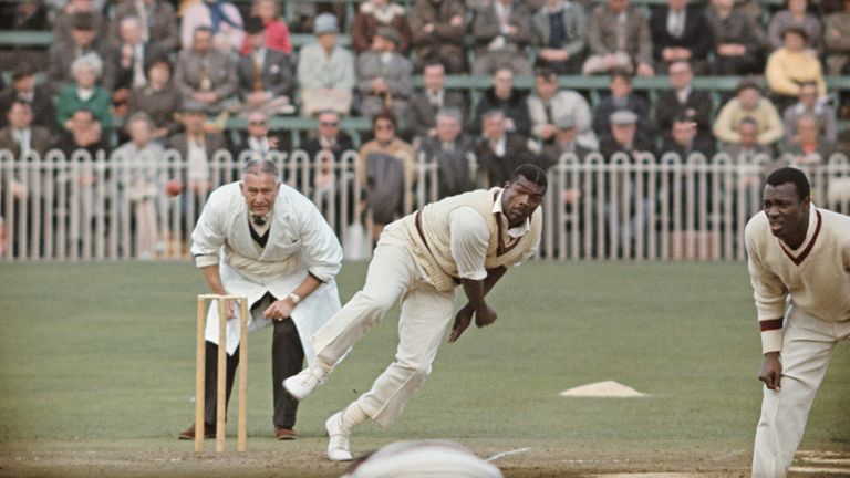 Charlie Griffith in action as umpire Syd Buller and Wes Hall (r) look on during a tour match of England in 1966